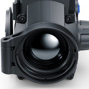 Close-up of a black thermal imaging scope or camera lens housing with a large objective lens, shown on a light gray background.