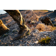 A person wearing camouflage pants and Nano X1 Adventure Tactical boots on rocky terrain