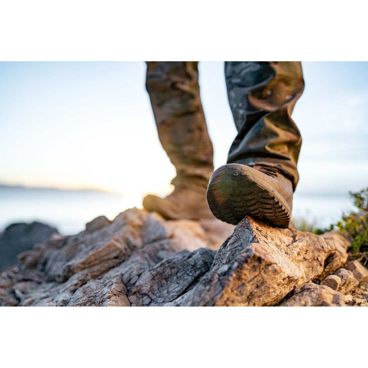 Close-up of feet wearing Nano X1 Adventure Tactical Boot stepping on rocks with a natural landscape
