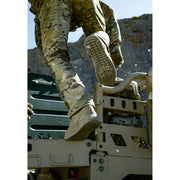 Person in military camouflage gear climbing onto a vehicle with rocky terrain in the background