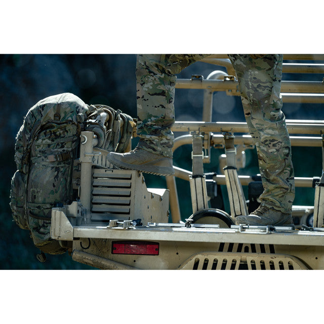 Person in military gear climbing onto a vehicle with a backpack